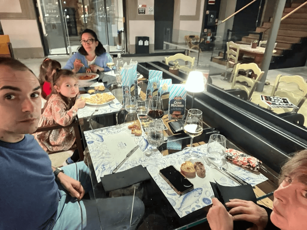 A group of people sitting at a long table in the Covered Market of Ravenna during a birthday dinner